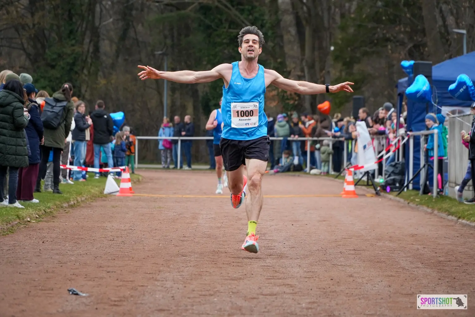 Alexander Büttner crossing the finish line at the Forstenrieder Volkslauf in March 2026 with both arms extended